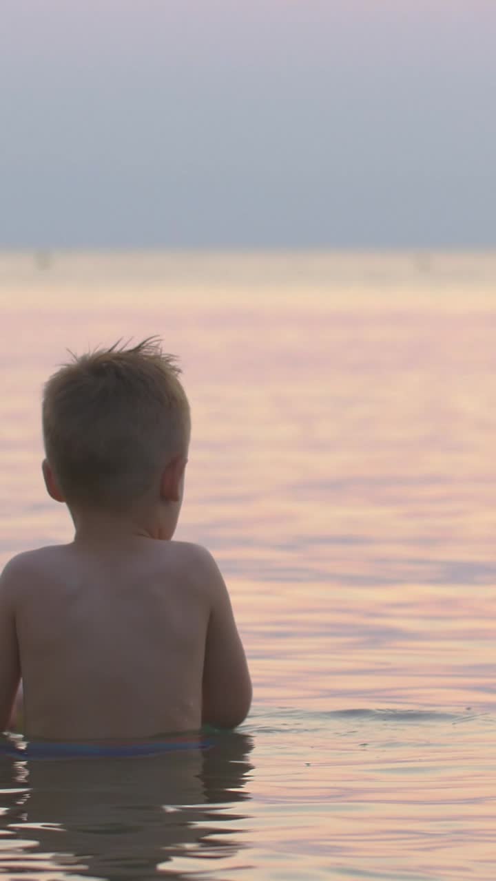 Child playing with toy boat in the sea at sunset