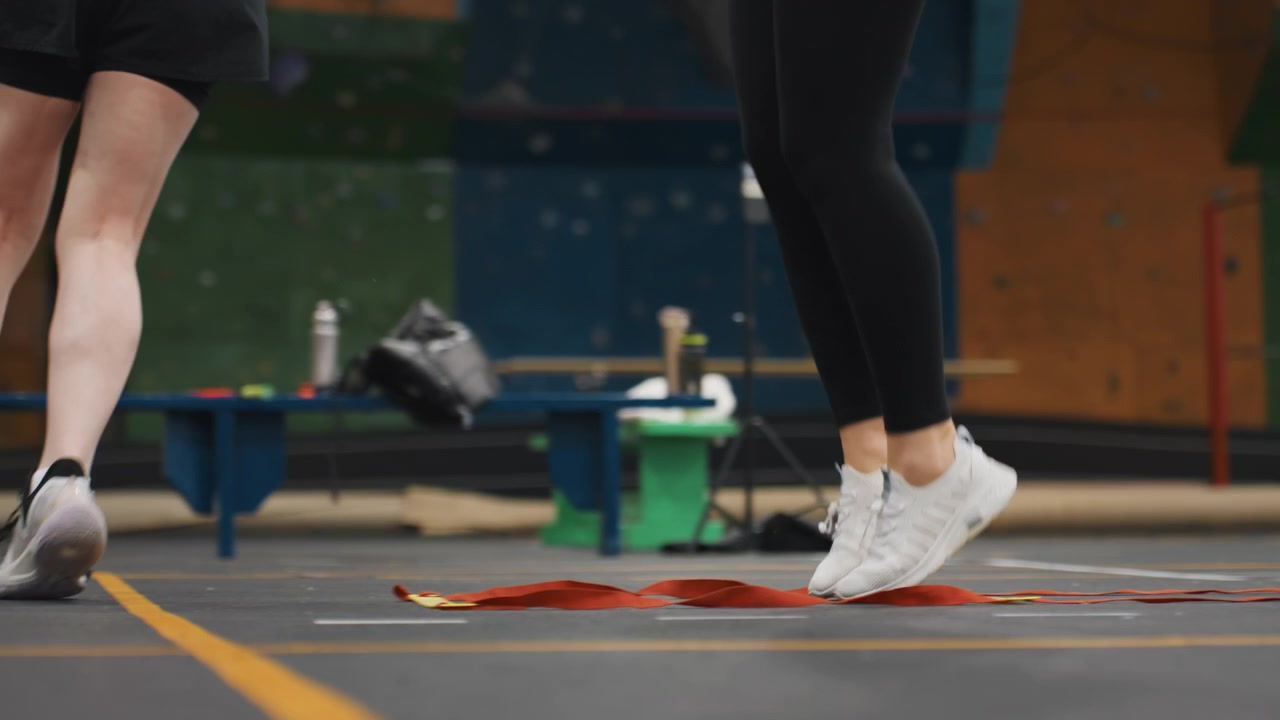 Primo piano di allenamento con scaletta per il gioco di gambe nel badminton, focalizzato su piedi veloci e atterraggi precisi sui pioli segnati, scarpe da ginnastica dinamiche che toccano i marcatori a corda su un campo al coperto, enfasi su ritmo e velocità.