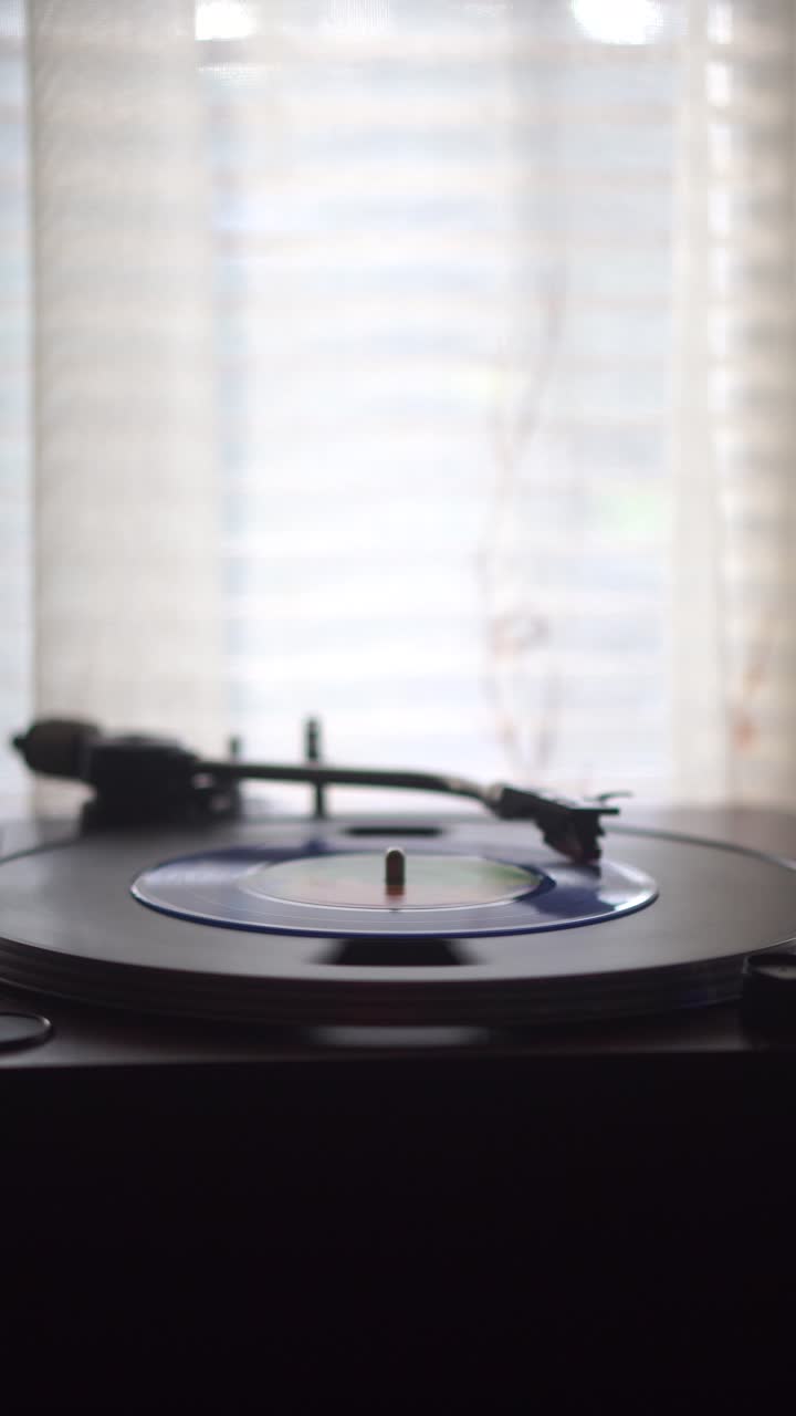 Vista verticale, disco in vinile blu singolo che gira su un giradischi vicino alla finestra.