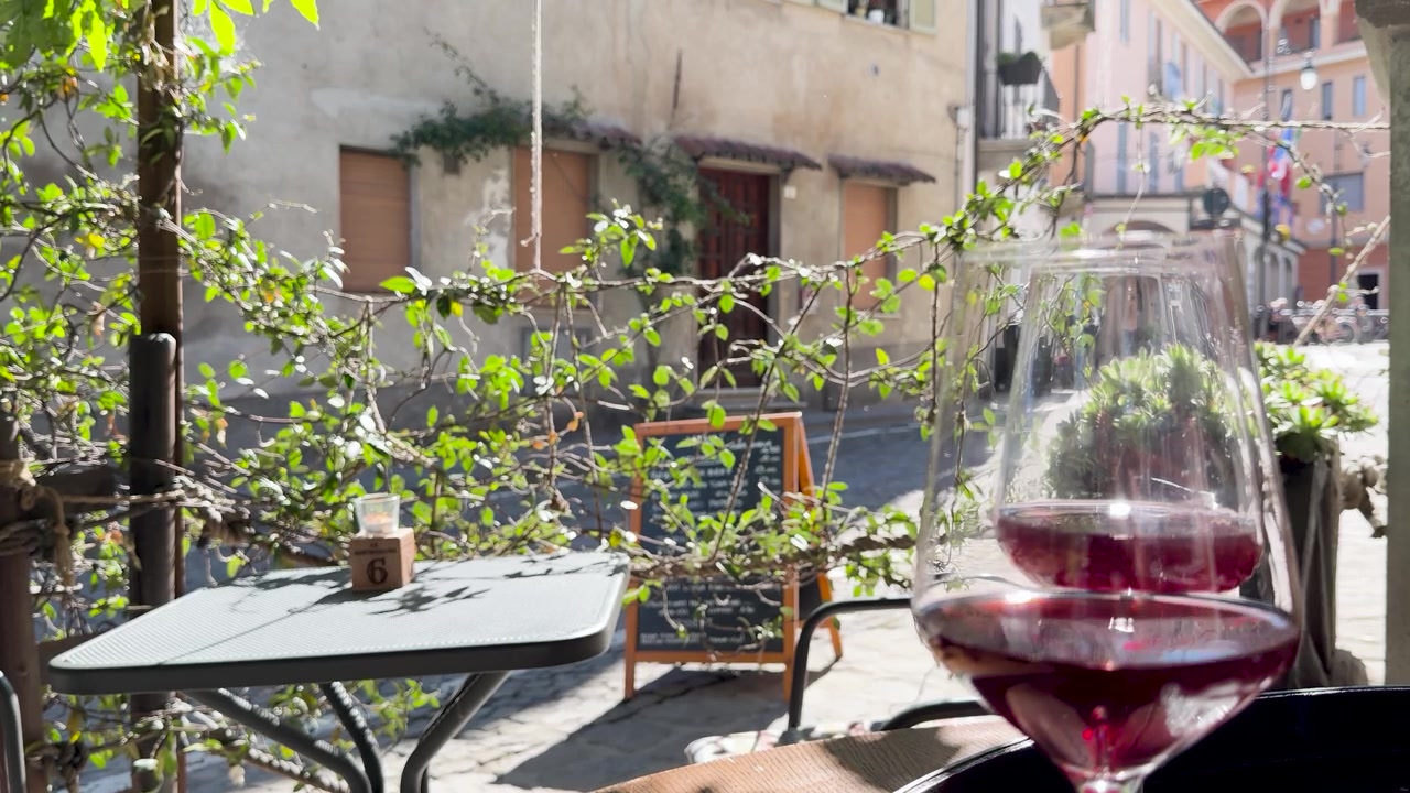 Un bicchiere di vino rosso è posato su un tavolo da caffè all'aperto e soleggiato in Piemonte, Italia.