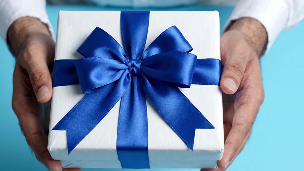 A beautifully wrapped gift box with a luxurious blue ribbon, held carefully in two hands against a soft blue background, ready to be given to someone special.