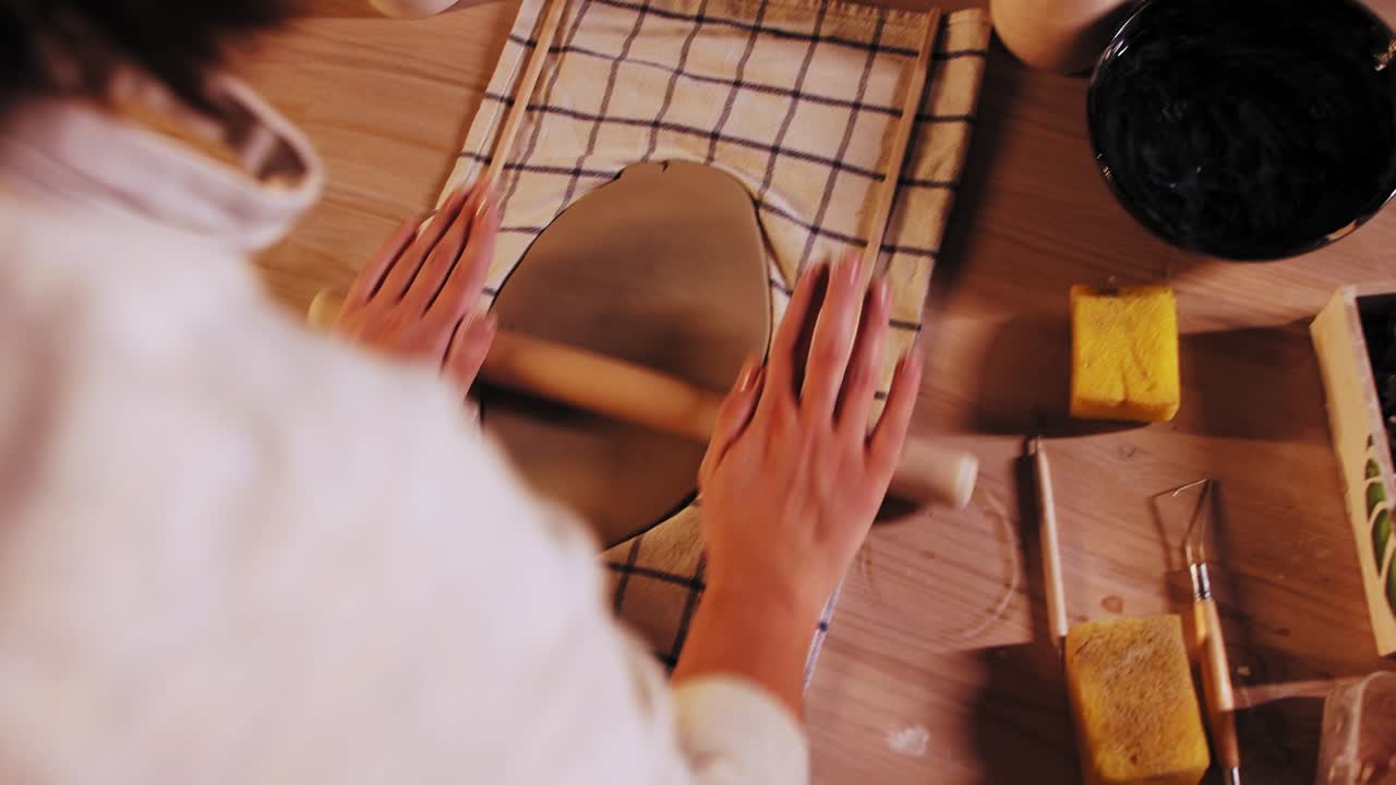 스튜디오 의 도자기 - 젊은 여성 도자기 가 롤링 핀 을 사용 하여 점토 의 조각 을 평평 하게 만드는 것