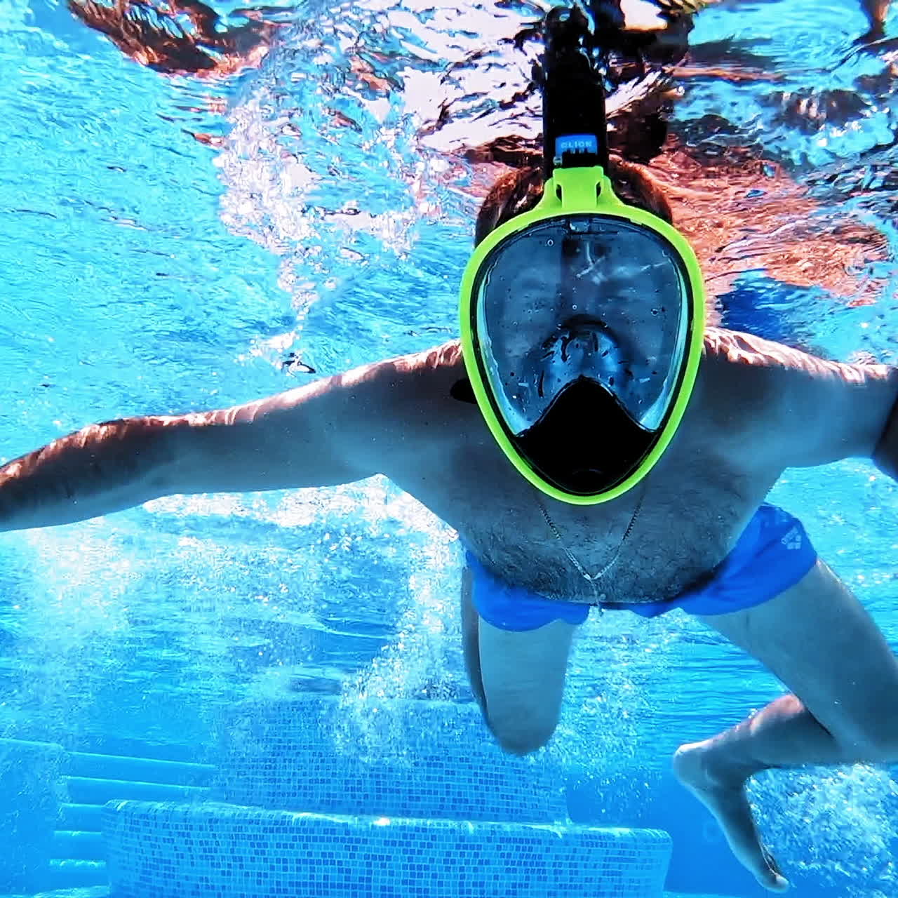 Underwater background of a swimming pool. A man in yellow mask swimming inside the clear blue water of a pool.