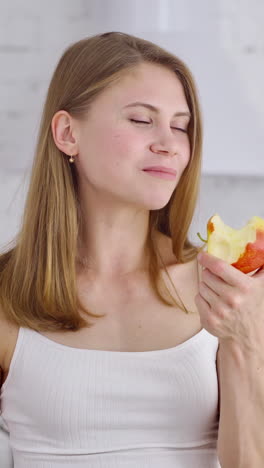 half-length portrait of young woman with apple. beautiful girl is eating a fresh organic fruit in the kitchen. healthy food. dieting concept. vertical video