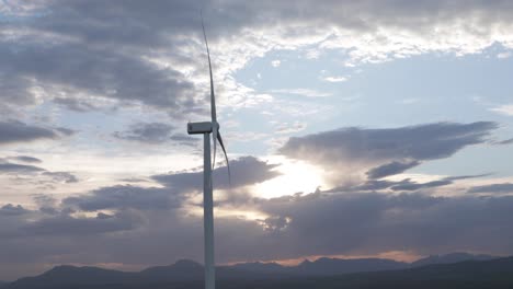 aerogenerador de giro lento con puesta de sol detrás de las nubes en el fondo