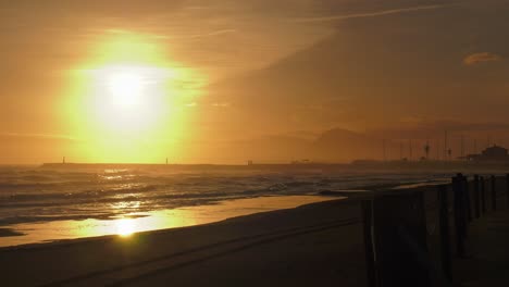 Brumoso-Amanecer-Sobre-La-Playa-De-Arena-Y-El-Puerto,-Olas-Rodando,-Oliva,-Costa-Mediterránea,-España