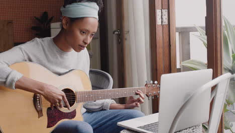 young woman playing guitar at home aspiring musician learning to play musical instrument using laptop enjoying creative expression practicing music