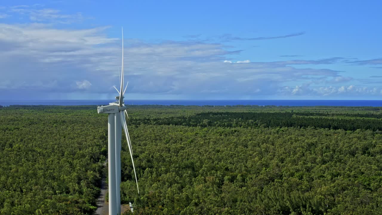 Side drone view of line of wind turbines in lush forest landscape, pretty sky