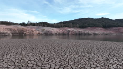 drone flying low over cracked soil ground on dried lake shores of sau swamp in catalonia, spain