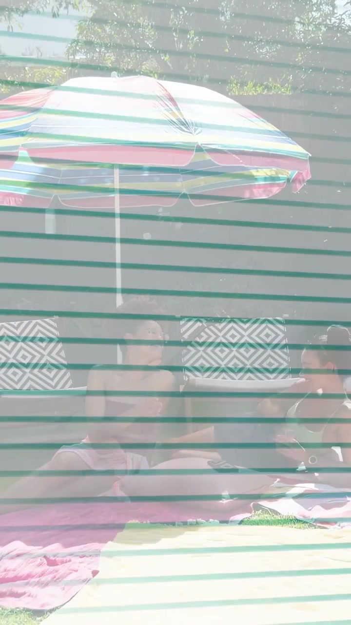 Vertical video: Two adults sitting under umbrella, camera pulling back revealing lawn for brands