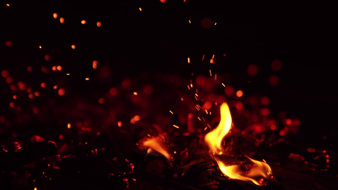 Tapping by the hot smoldering embers. Bright sparks fly up and little flames appear. Close up.