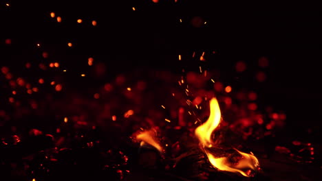 tapping by the hot smoldering embers. bright sparks fly up and little flames appear. close up.