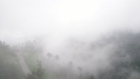 flying rising through clouds, aerial in the middle of the clouds above a mountain forest road landscape