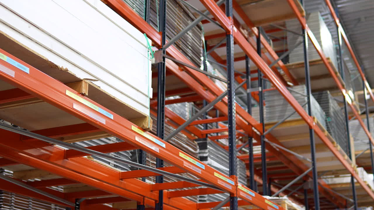 Primo piano di scaffali industriali in metallo arancione che contengono grandi pile di pannelli di legno e compensato in un centro di distribuzione legname professionale o magazzino di ferramenta