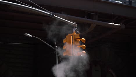 yellow traffic light in a dark background with steam coming out of the streets in new york city.