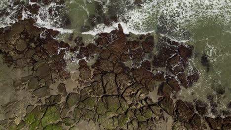 aerial view topdown waves break over rocky shoreline ascending aerial