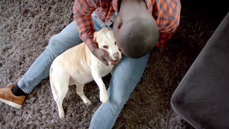 happy african american man sitting on floor at home, petting his pet dog, slow motion