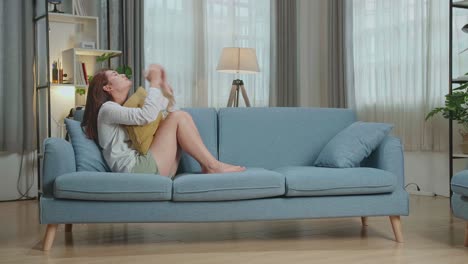 woman sitting on a couch looking sad and covering her face with a pillow.