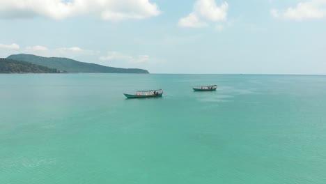 barcos de pesca amarrados y descansando sobre hermosas aguas azules claras en la bahía sarracena en koh rong sanloem, camboya - toma aérea en órbita de ángulo bajo