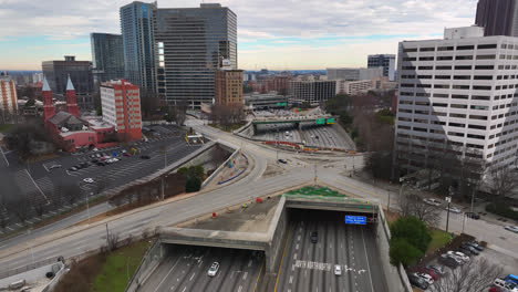 Cinematic-aerial-view-of-cars-driving-on-multi-lane-road-in-Atlanta-city,-Atlanta-freeway-traffic,-Historical-Folk-Art-Park-on-Peachtree-street-with-Roman-Catholic-church-in-the-view,-Georgia,-USA