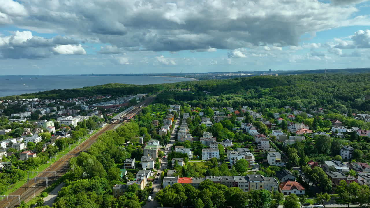 Aerial view of a coastal city with residential homes, lush forests, and a railway line