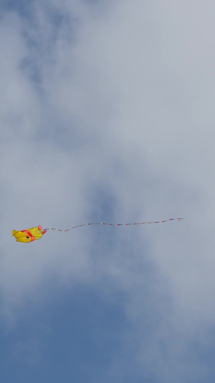 Un aquilone giallo con una coda vivace si libra nel cielo parzialmente nuvoloso in una giornata estiva ventosa.