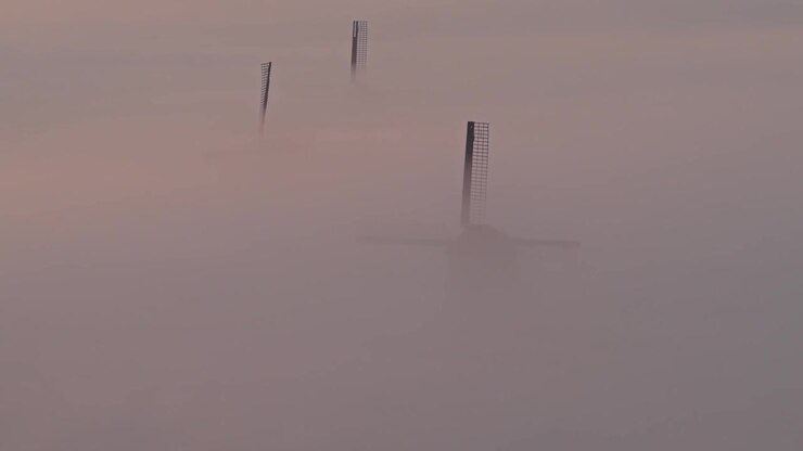Wind turbines emerging from thick morning fog at sunrise