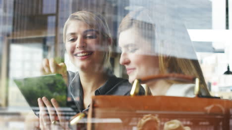 Two-woman-friends-sharing-coffee-using-digital-tablet-in-cafe