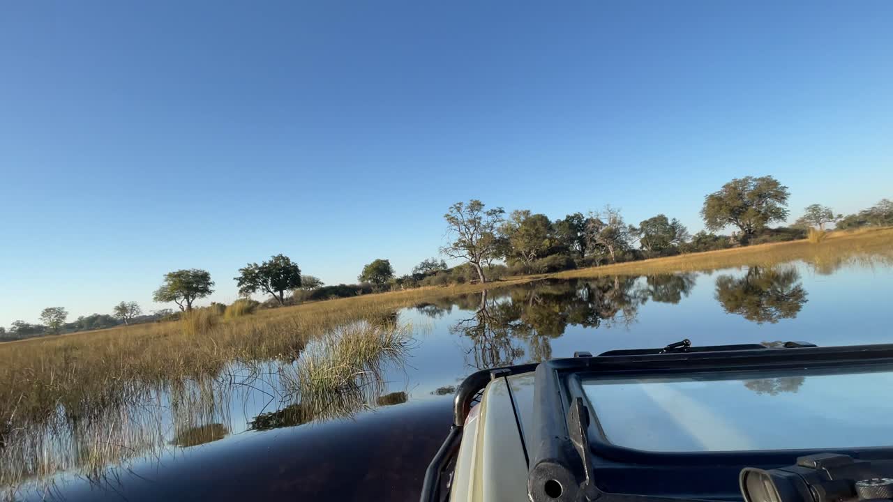 A safari vehicle navigates through a shallow water crossing in Africa, blending adventure with the raw beauty of the wilderness