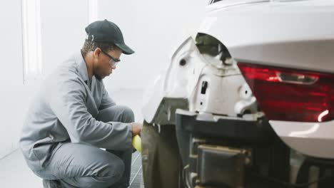 African-American-male-car-mechanic-kneeling-by-a-car-and-repairing-it-