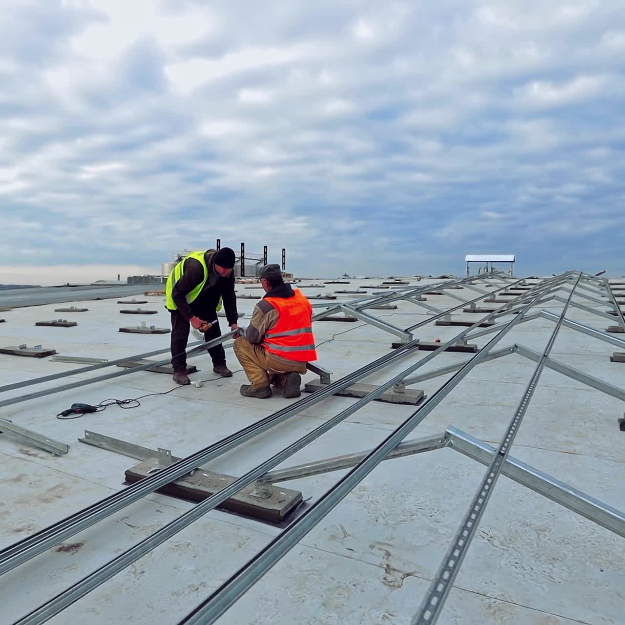 Installation of solar power plant on flat roof. Workers attach metal basis for photovoltaic solar panels under the beautiful sky.