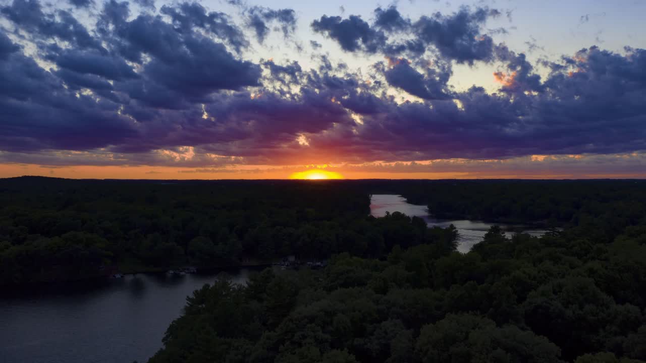 la hora dorada del atardecer brilla sobre un lago tranquilo y un bosque con silueta, aérea