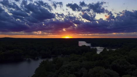 golden hour sunset glow over a calm lake and a silhouetted forest, aerial