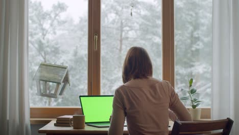 relaxed woman working on computer at home by wooden window slow motion. back portrait of girl typing on laptop drinking coffee tea for relaxation. lockdown quarantine stay at home concept