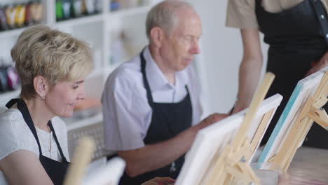 side view of a happy senior people smiling while drawing as a recreational activity or therapy in paint class together with the group of retired women and men