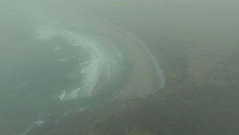 drone flying out of the clouds towards the beautiful keel beach on achill island