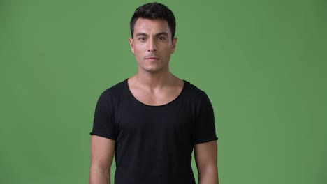 young handsome hispanic man against green background