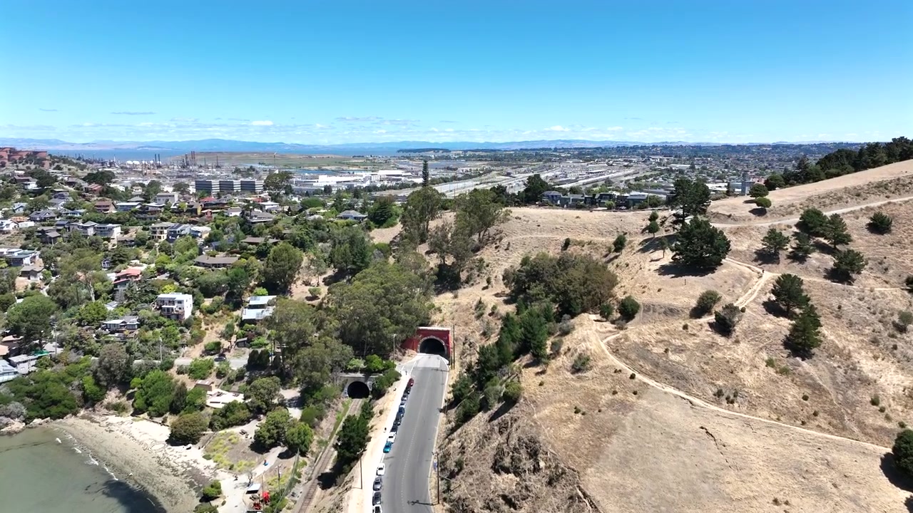 Riprese aeree con drone in avanzamento e ascesa sopra la collina di Point Richmond e il quartiere residenziale a Richmond, California. La telecamera rivela la raffineria Chevron di Richmond e un'estesa rete ferroviaria