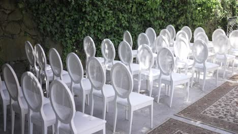 white chairs arranged for an outdoor event against an ivy-covered stone wall