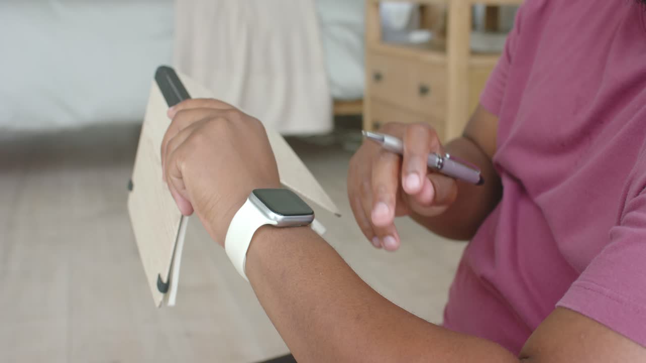 African man placing journal on stand taking notes with pen in bedroom checking watch copy space