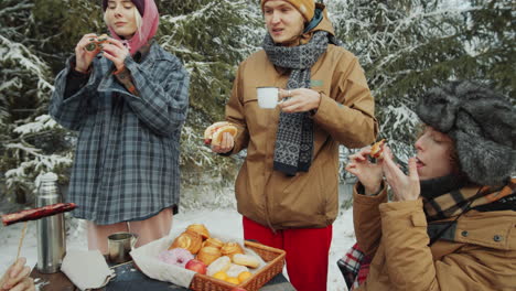 friends having meal at campsite in winter forest