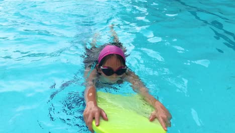 Niña-Asiática-Usando-Patineta-En-La-Piscina,-Nadando-Directamente-A-La-Cámara.