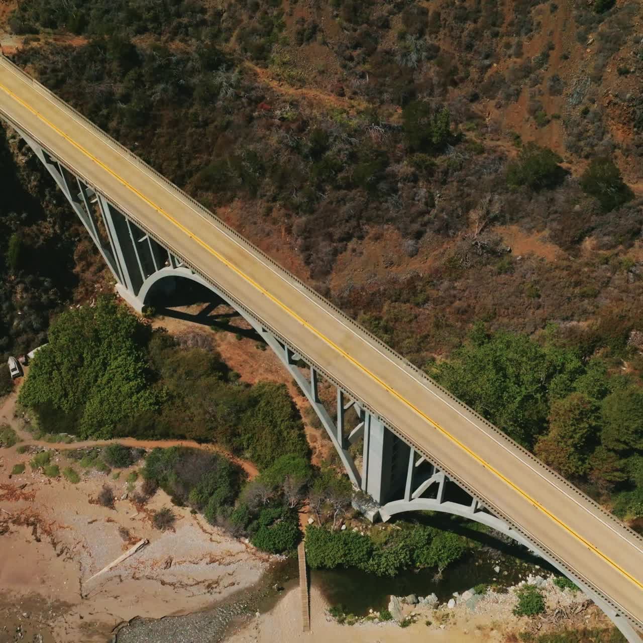 Mountains connected by the arch bridge with cars moving by. Drone descending above the rocks covered with moss