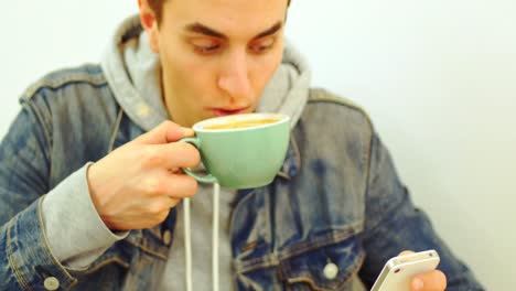 Man-using-mobile-phone-while-drinking-cup-of-coffee