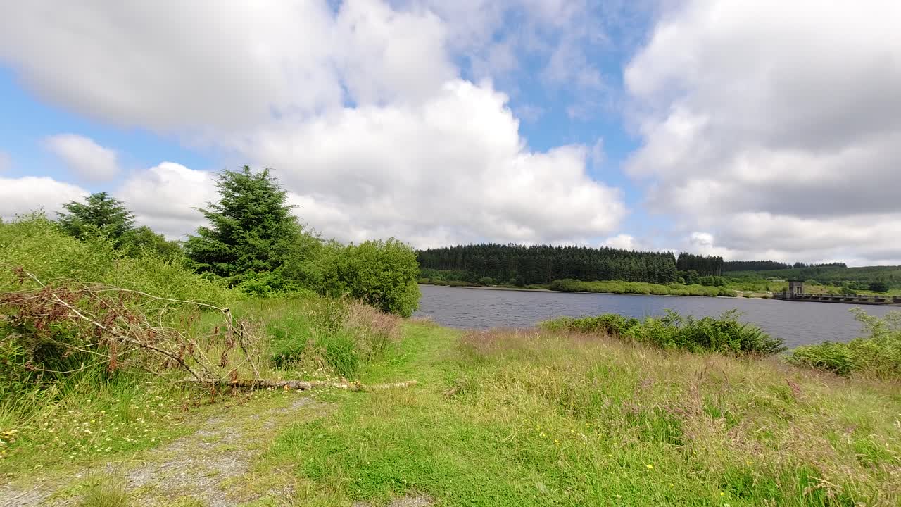sunny alwen embalse timelapse nubes rápidas que pasan sobre el vasto agua azul del lago del bosque hacia el espectador