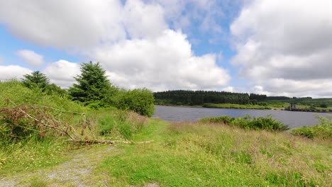 Sunny-Alwen-Embalse-Timelapse-Nubes-Rápidas-Que-Pasan-Sobre-El-Vasto-Agua-Azul-Del-Lago-Del-Bosque-Hacia-El-Espectador