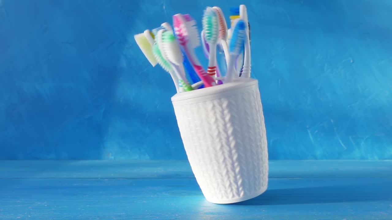 muchos cepillos de dientes diferentes en una taza blanca giran en una mesa contra un fondo azul. video de bucle crudo creativo 4k con la capacidad de disminuir aún más. filmado en cámara de cine de alta velocidad, 1000 fps.