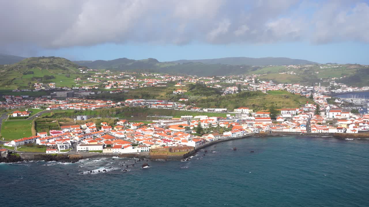 Città costiera di Faial con edifici bianchi, tetti rossi e vecchi vulcani sullo sfondo.