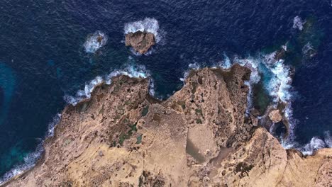 vista de arriba hacia abajo sobre una línea de costa rocosa en la bahía de dwejra, con olas salpicando