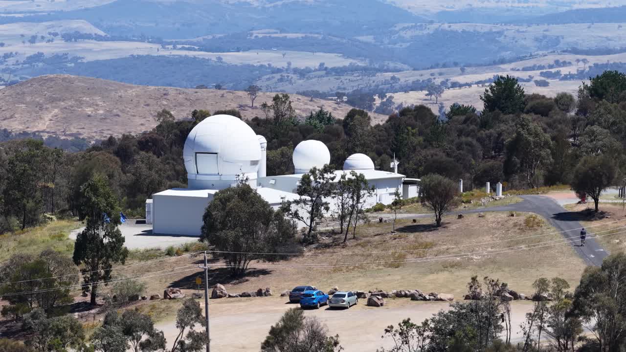 Wide static shot of white astronomical observatory domes on a hill under bright daylight